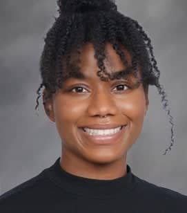 A headshot of an African American woman smiling. She is wearing a black shirt with her hair in a bun